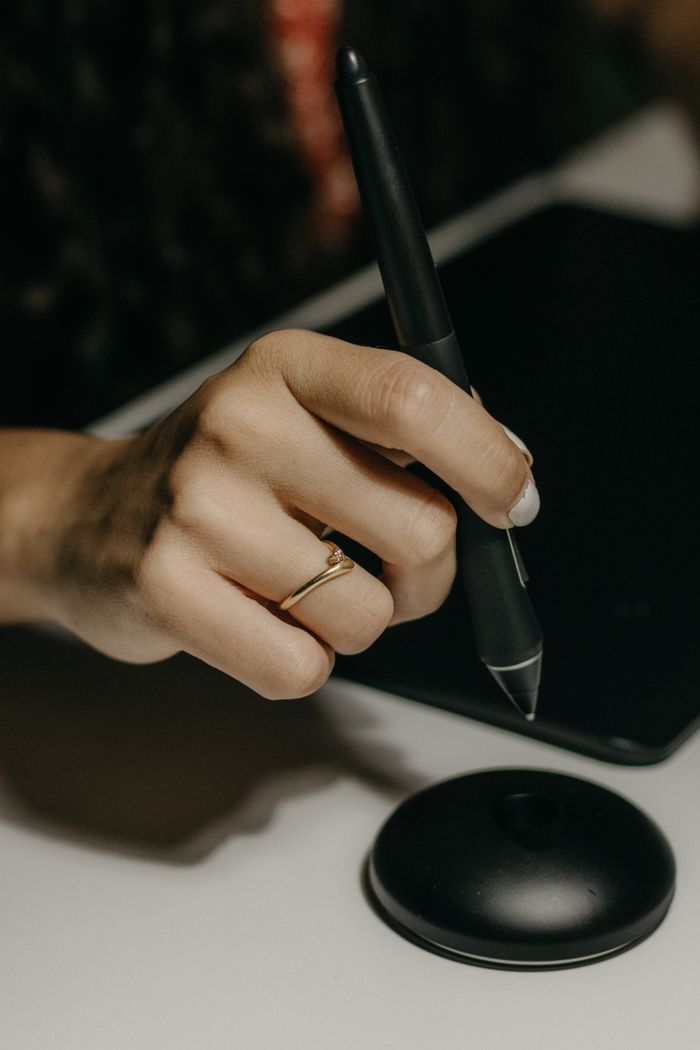 brand-03 A woman's hand with a ring using a stylus on a digital tablet, focused close-up.