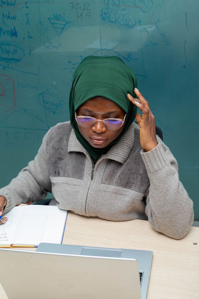 digital A woman in a headscarf and eyeglasses studying with a laptop and notes.